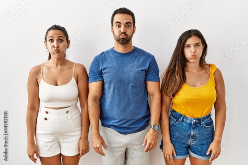 Group of young hispanic people standing over isolated background puffing cheeks with funny face. mouth inflated with air  crazy expression.