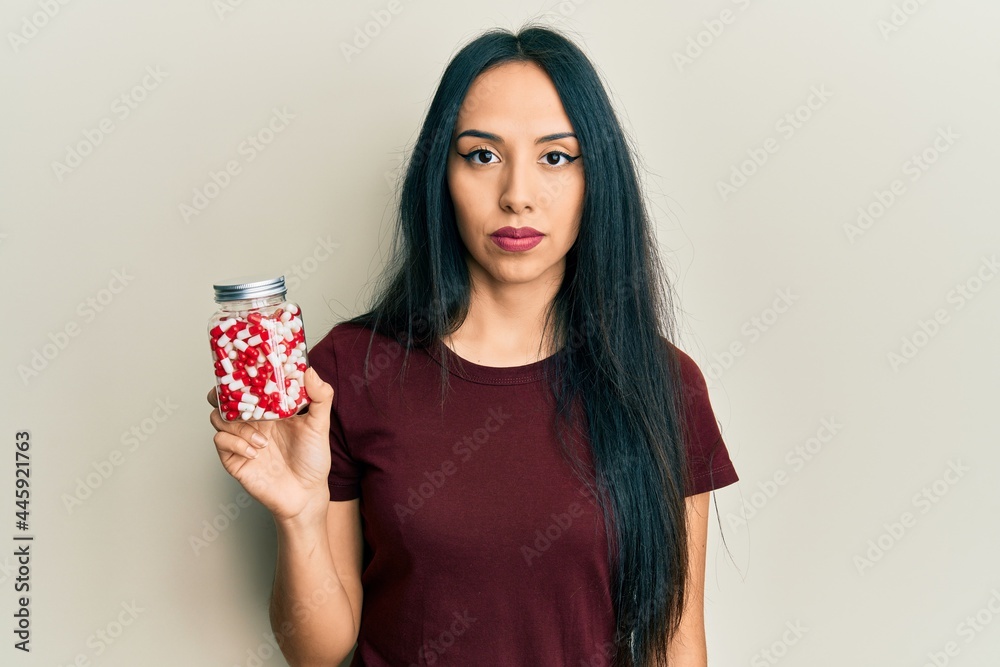 Young hispanic girl holding pills thinking attitude and sober expression looking self confident Young hispanic girl holding pills thinking attitude and sober expression looking self confident