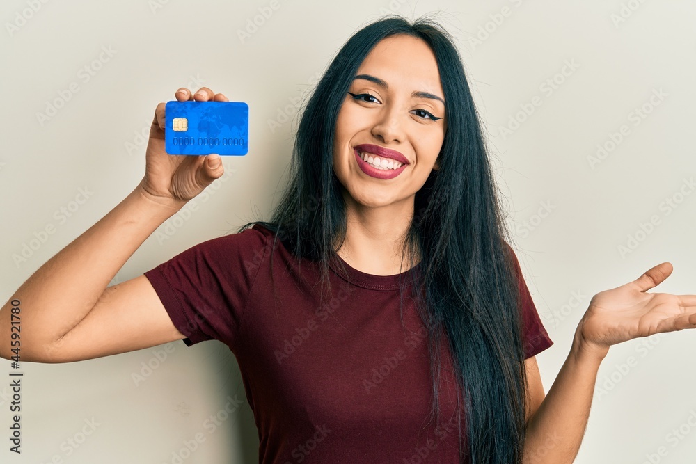 Young hispanic girl holding credit card celebrating achievement with happy smile and winner expression with raised hand Young hispanic girl holding credit card celebrating achievement with happy smile and winner expression with raised hand
