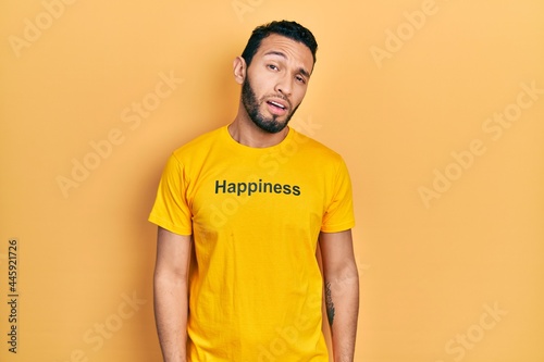 Hispanic man with beard wearing t shirt with happiness word message looking sleepy and tired, exhausted for fatigue and hangover, lazy eyes in the morning.