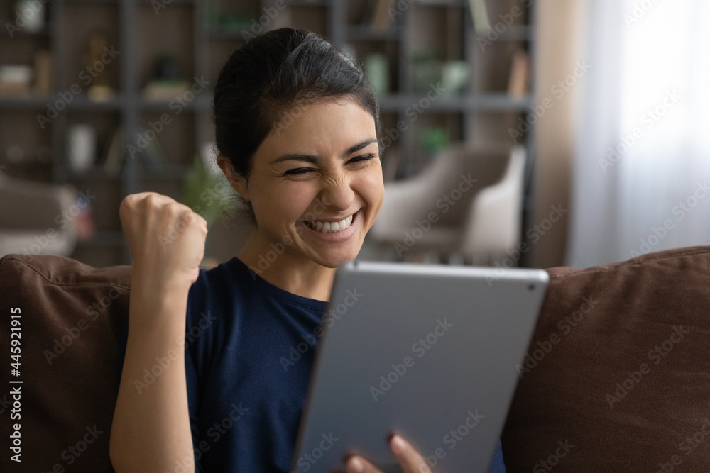 Overjoyed millennial Indian woman look at table screen feel euphoric with online victor or win on gadget. Excited happy young biracial female triumph read good news on pad device. Success concept. Overjoyed millennial Indian woman look at table screen feel euphoric with online victor or win on gadget. Excited happy young biracial female triumph read good news on pad device. Success concept.