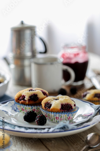 Muffins con more in primo piano su piattino decorato bianco e blu e sullo sfondo sfocato tazze confettura caffettiera sfocati photo