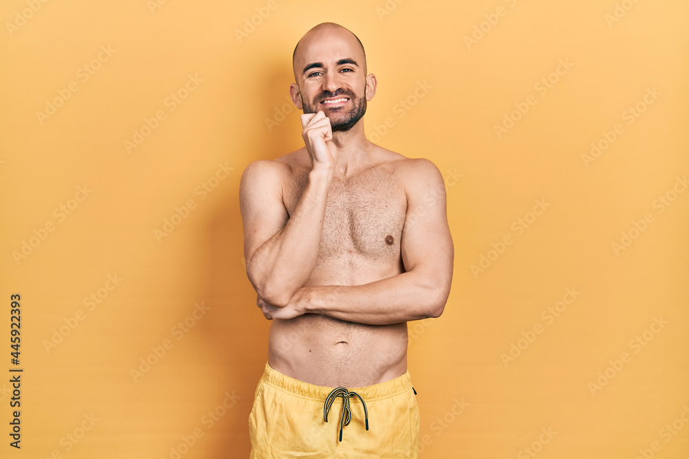 Fototapeta premium Young bald man wearing swimwear looking confident at the camera with smile with crossed arms and hand raised on chin. thinking positive.