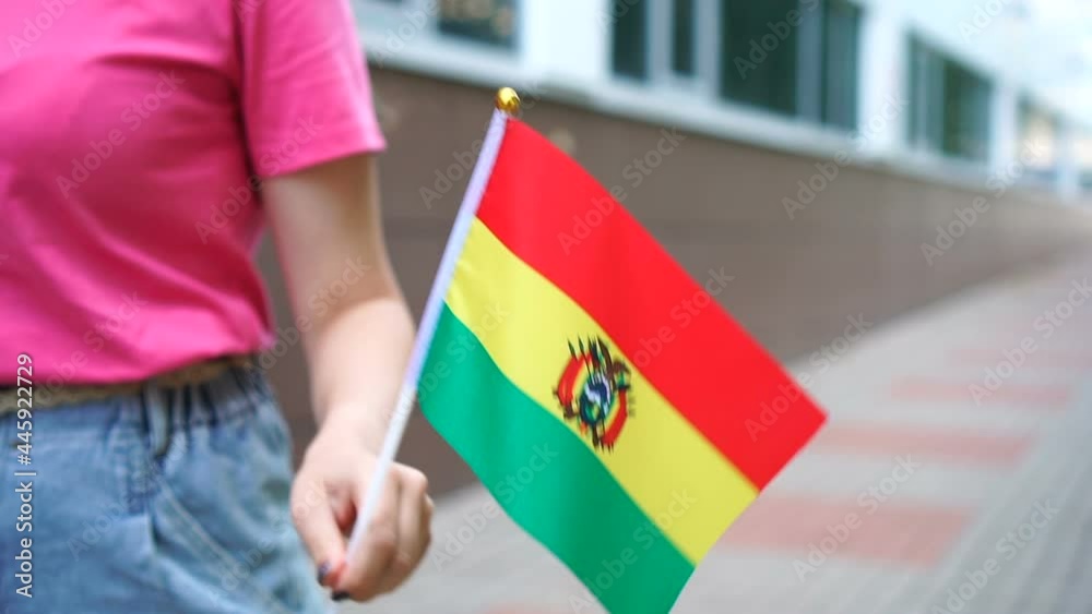 Unrecognizable woman holding Bolivian flag. Girl walking down street with national flag of Bolivia