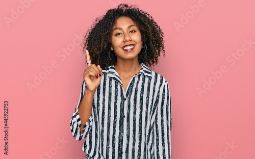 Young african american girl wearing casual clothes showing and pointing up with finger number one while smiling confident and happy. © Krakenimages.com