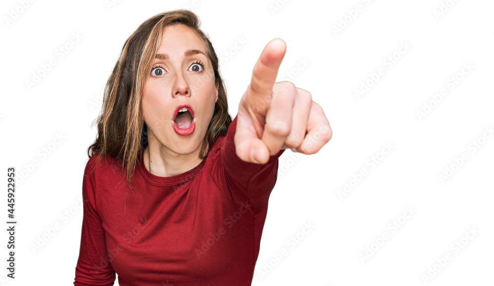 Young blonde woman wearing casual clothes pointing with finger surprised ahead, open mouth amazed expression, something on the front Young blonde woman wearing casual clothes pointing with finger surprised ahead, open mouth amazed expression, something on the front