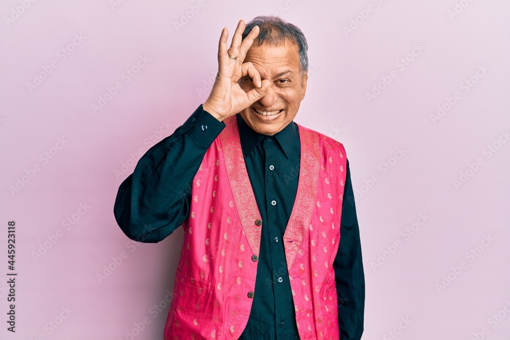 Middle age indian man wearing traditional indian clothes doing ok gesture with hand smiling, eye looking through fingers with happy face. Middle age indian man wearing traditional indian clothes doing ok gesture with hand smiling, eye looking through fingers with happy face.