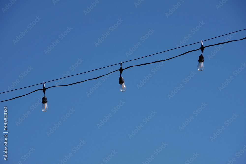 Segment of outdoor lighting with lightbulbs hanging from a wire under blue sky