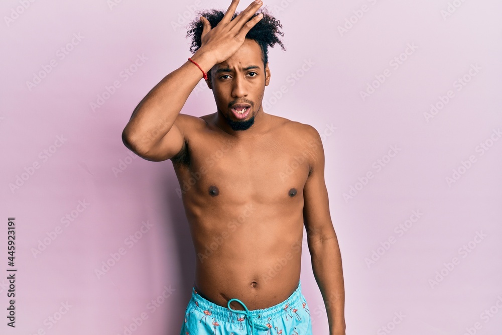 Fototapeta premium Young african american man with beard wearing swimsuit surprised with hand on head for mistake, remember error. forgot, bad memory concept.