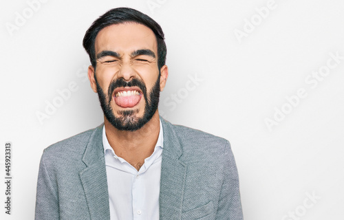 Young hispanic man wearing business clothes sticking tongue out happy with funny expression. emotion concept.