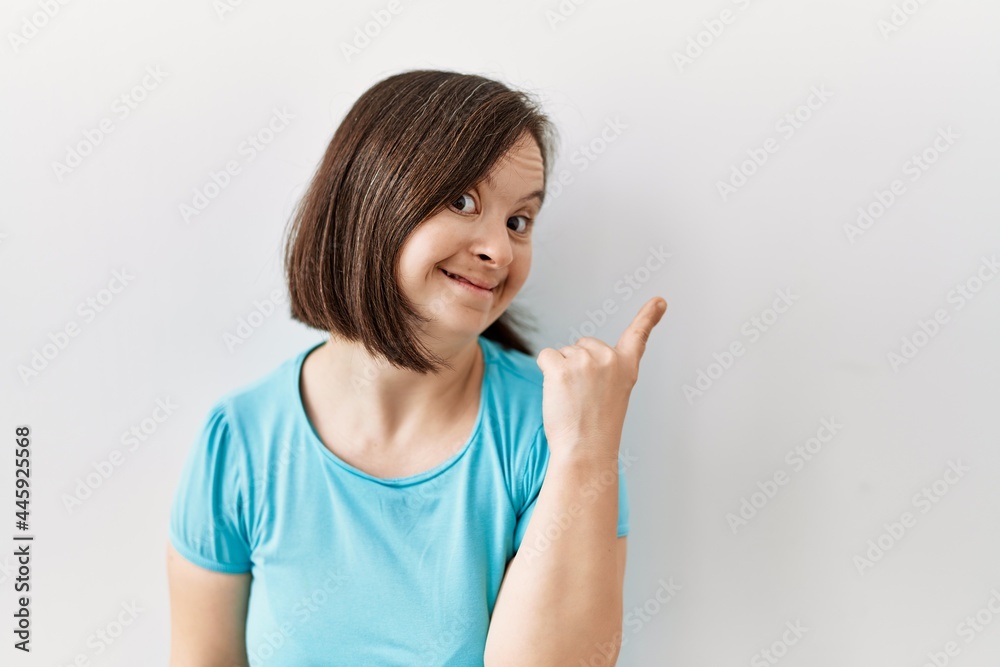 Young down syndrome woman standing over isolated background with a big smile on face, pointing with hand and finger to the side looking at the camera. Young down syndrome woman standing over isolated background with a big smile on face, pointing with hand and finger to the side looking at the camera.