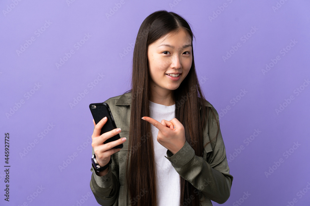 Young Chinese girl using mobile phone over isolated purple background and pointing it Young Chinese girl using mobile phone over isolated purple background and pointing it