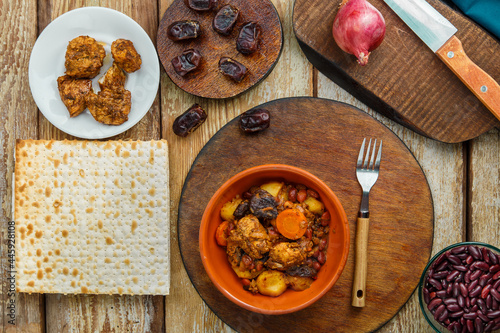 Jewish dish chelnt with meat on the table in a plate near ingredients and matzo. photo