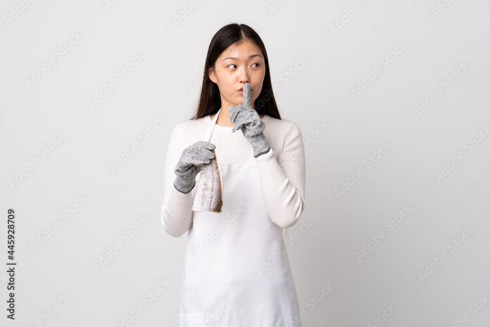 Chinese fishmonger wearing an apron and holding a raw fish over isolated white background showing a sign of silence gesture putting finger in mouth Chinese fishmonger wearing an apron and holding a raw fish over isolated white background showing a sign of silence gesture putting finger in mouth