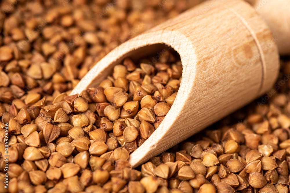 Obraz premium A wooden ladle lies on a brown buckwheat. Close-up.