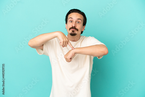 Young caucasian man isolated on blue background making the gesture of being late