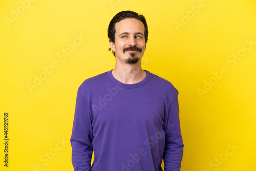 Young caucasian man isolated on yellow background having doubts while looking side