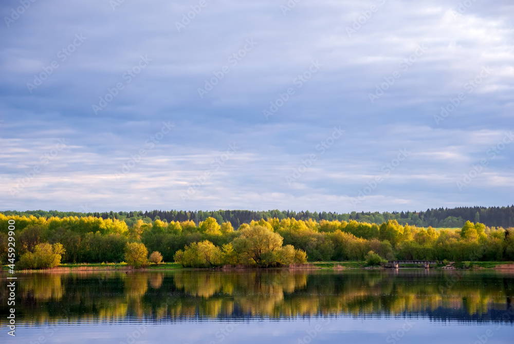 Autumn landscape with lake, trees with yellow leaves and sky with beautiful clouds.