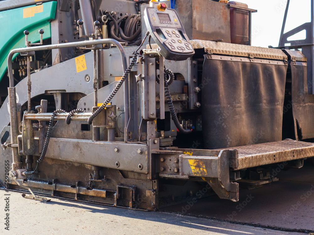 Close-up back view of an road paver in the process of paving asphalt.