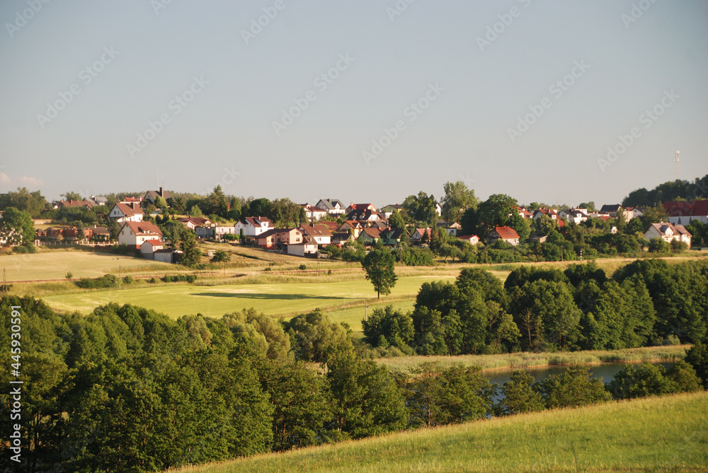 Tiny village with white houses and red roofs among green fields and meadows
