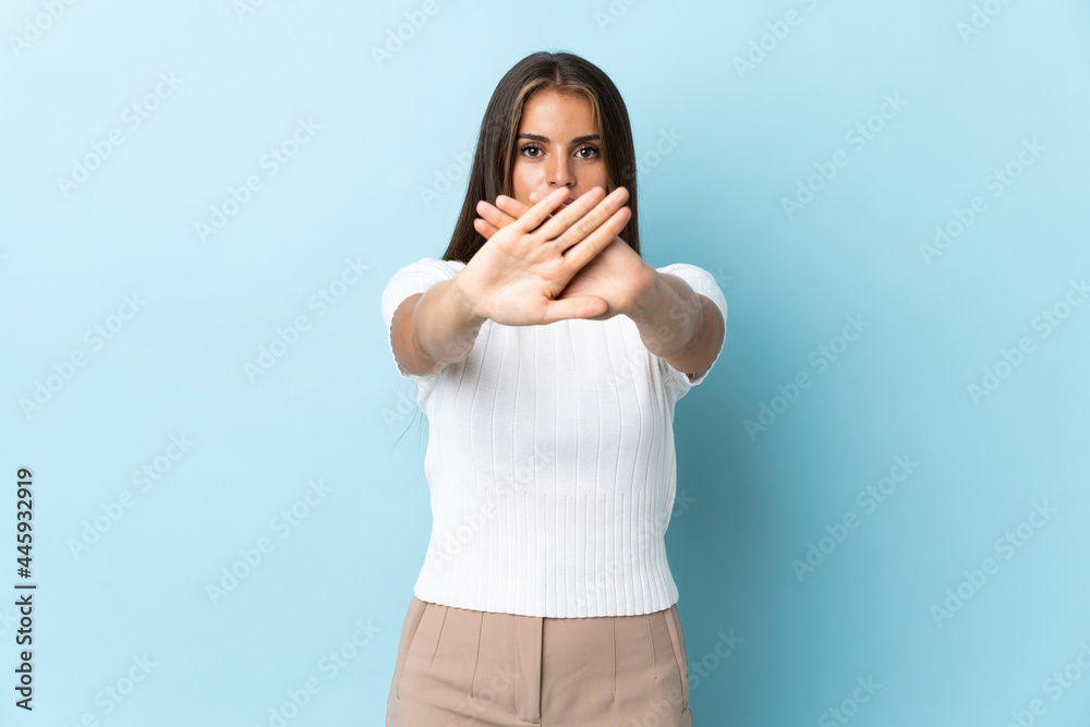 Young Uruguayan woman isolated on blue background making stop gesture with her hand to stop an act Young Uruguayan woman isolated on blue background making stop gesture with her hand to stop an act