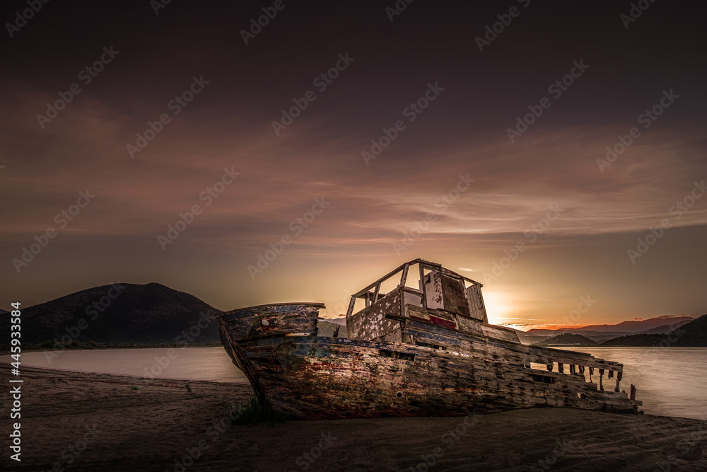 An old abandoned shipwreck, wrecked boat sunken ship stand on beach coast. Scenic sunset sky. Old Fishing Boat Wreck.