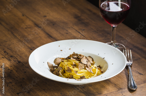 Pasta with truffles and glass of red wine on wooden table copy space.	