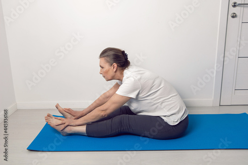 elderly woman does yoga on a blue rug in a white room at home © saulich84