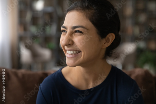 Close up of excited millennial Indian woman look in distance laugh at funny joke. Smiling young mixed race ethnicity female have fun dream or think of future success perspectives. Humor concept.