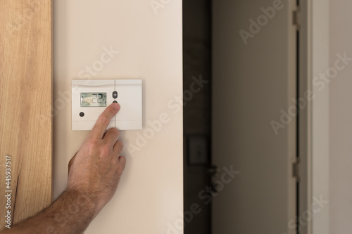 Male hand pushing the button of home heating and cooling system control unit