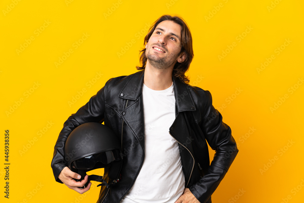 Man with a motorcycle helmet isolated on yellow background thinking an idea while looking up Man with a motorcycle helmet isolated on yellow background thinking an idea while looking up