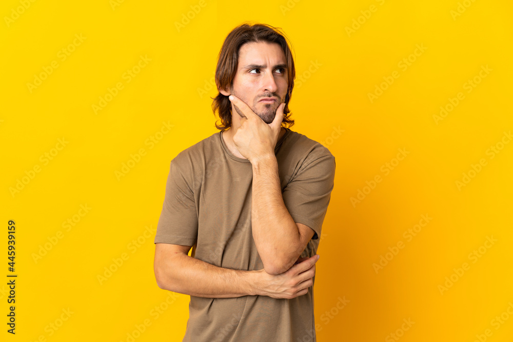 Young handsome man isolated on yellow background having doubts and with confuse face expression Young handsome man isolated on yellow background having doubts and with confuse face expression