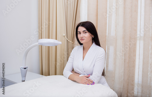 a beautiful beautician in a white uniform is sitting near the couch in the office © Яна Айбазова