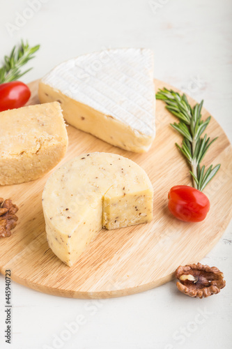 Cheddar and various types of cheese with rosemary and tomatoes on wooden board on a white background . Side view, selective focus.