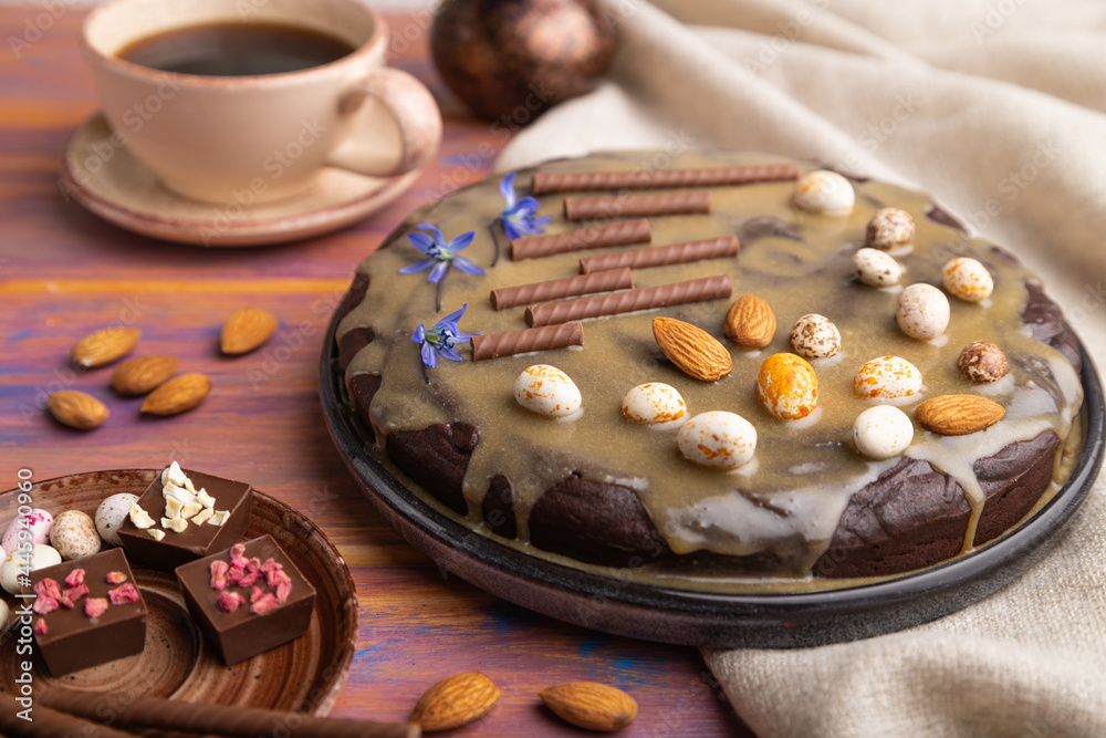 Homemade chocolate brownie cake with caramel cream and almonds with cup of coffee on a colored wooden background. Side view, selective focus. Homemade chocolate brownie cake with caramel cream and almonds with cup of coffee on a colored wooden background. Side view, selective focus.