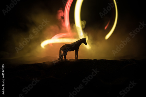 Beautiful horse running in desert at night. Silhouette of a horse miniature standing at foggy night. Creative table decoration with colorful backlight with fog. Selective focus