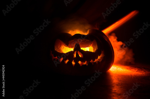 Close up view of scary Halloween pumpkin with eyes glowing inside at black background. Selective focus
