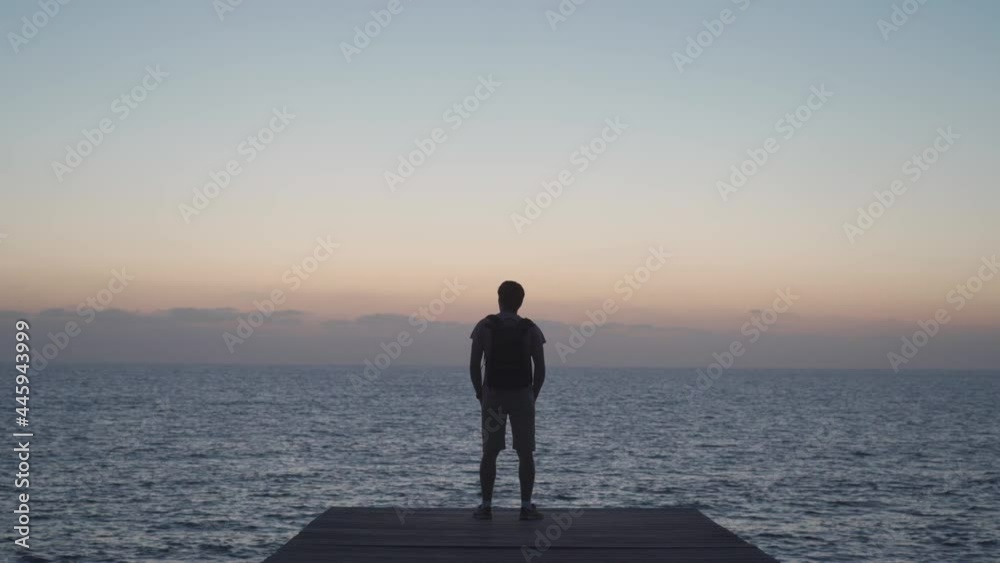 Silhouette of man traveler with backpack enjoying sunset on wooden pier overlooking mediterranean sea on island of cyprus, city of paphos. Travel concept. Backpacker on wooden jetty overlooking ocean. Silhouette of man traveler with backpack enjoying sunset on wooden pier overlooking mediterranean sea on island of cyprus, city of paphos. Travel concept. Backpacker on wooden jetty overlooking ocean.