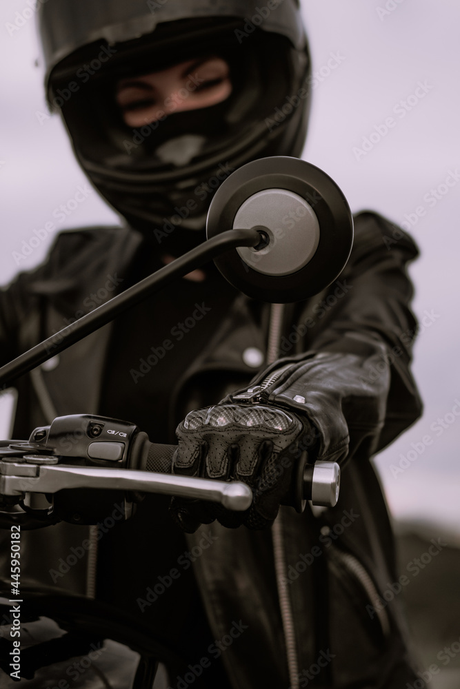 Obraz premium Stylish motorcyclist woman in helmet and leather jacket sitting on black motorcycle. Female driver outdoors on nature background. Trip, cafe racers, speed, freedom concept.