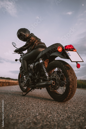 Stylish motorcyclist woman in helmet and leather jacket sitting on vintage motorcycle. Female driver outdoors on nature background. Trip  cafe racers  speed  freedom concept.