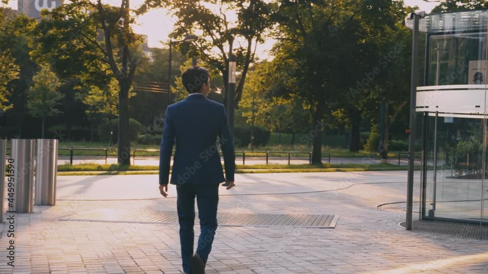 A back view of a person in a suit walks forward near an office building downtown. A businessman in a downtown city near skyscrapers thoughtfully looks around. Man in modern suit clerk in a jacket. A back view of a person in a suit walks forward near an office building downtown. A businessman in a downtown city near skyscrapers thoughtfully looks around. Man in modern suit clerk in a jacket.