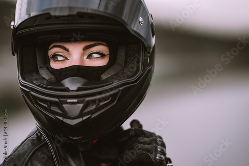 Portrait of confident motorcyclist woman in motorcycle helmet. Young driver biker looking away outdoors. Cafe racers, motorbike aesthetics and vintage design concept.