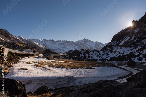 Mountain landscape with snow in Andes with sun in the horizon and an old train line not in use. Las Cuevas, Mendoza, Argentina 