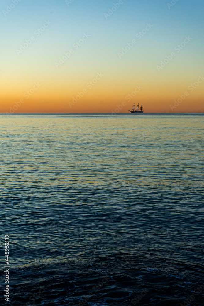 Sunrise at sea with a frigate on the horizon