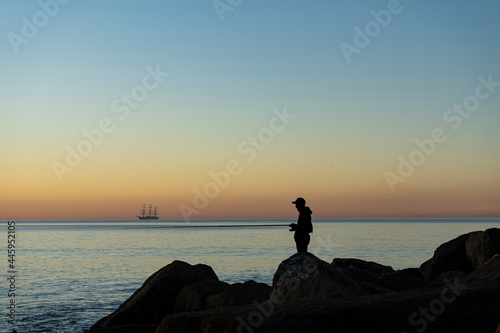 Fisherman silhouette at sunrise on breakwater © Martin