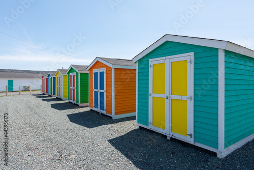 A row of small colorful painted huts or sheds made of wood. The exterior walls are colorful with double wooden doors. The sky is blue in the background and the storage units are sitting on gravel. © Dolores  Harvey