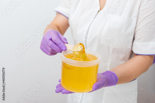 Natural honey sugar paste shugaring closeup. Women beautician holds jar wax of paste for sugar depilation shugaring, white background © kuzenkova