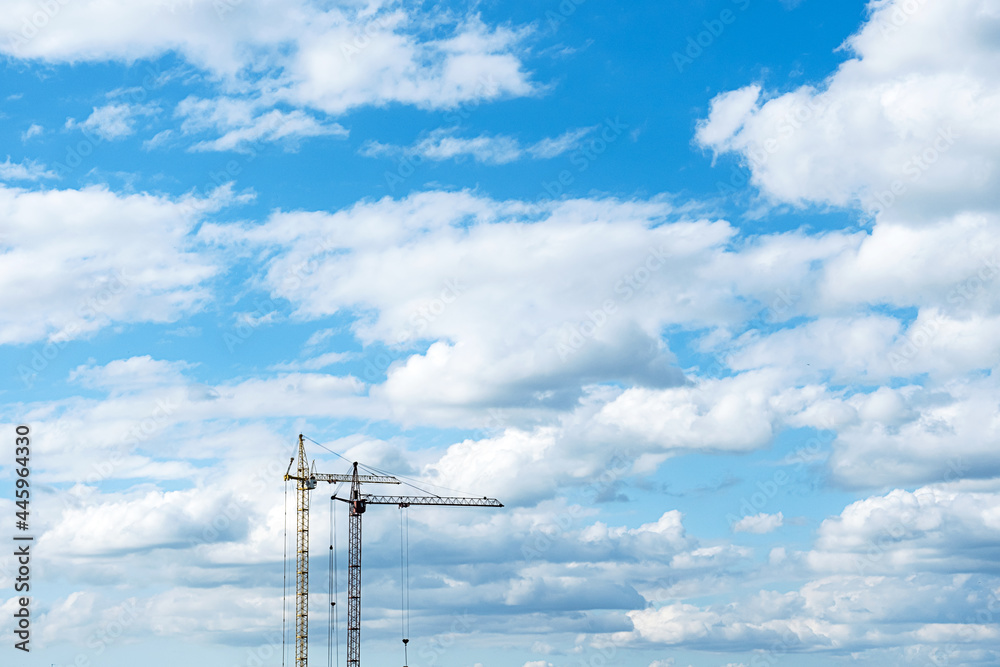 Two construction cranes against the blue cloudy sky. Tower crane for lifting loads in the construction of buildings. Industrial background with place for text or advertisement. Two construction cranes against the blue cloudy sky. Tower crane for lifting loads in the construction of buildings. Industrial background with place for text or advertisement.