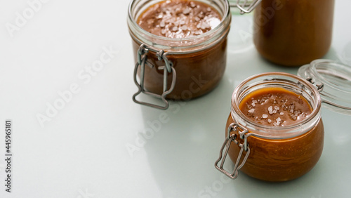 Salted caramel in glass jars on light neutral background. Brown caramel or condensed milk with sea salt crystalls. Long horizontal banner, copy space left photo