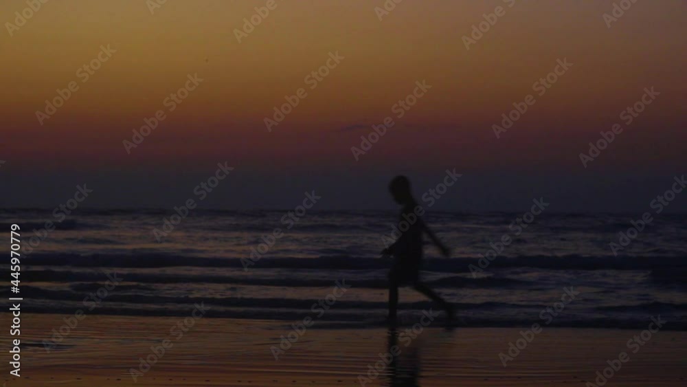 Silhouette of a child walking along the beach with the ocean and sky background Silhouette of a child walking along the beach with the ocean and sky background